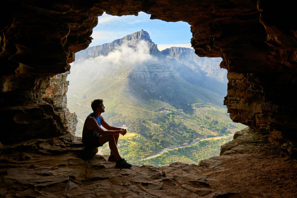 pexels-photo-1659437-1659437 A man sitting in a cave overlooking a majestic mountain landscape under daylight.